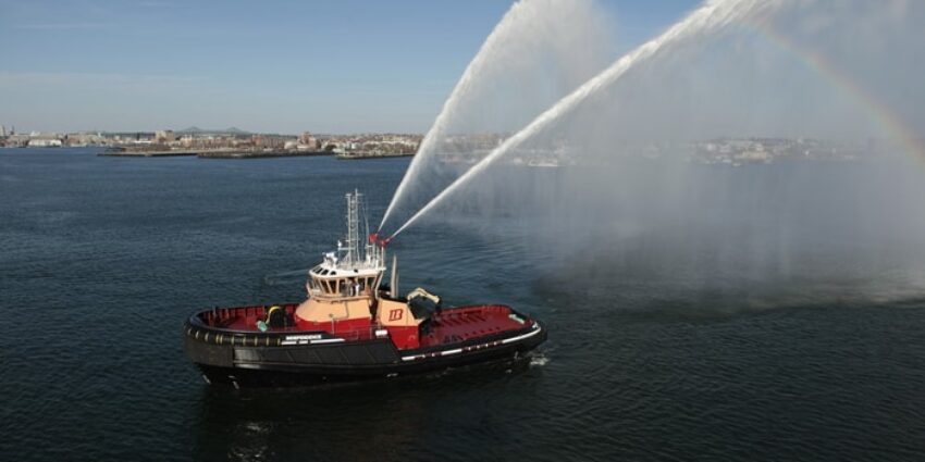 A red and white boat sprays streams of water while floating offshore.